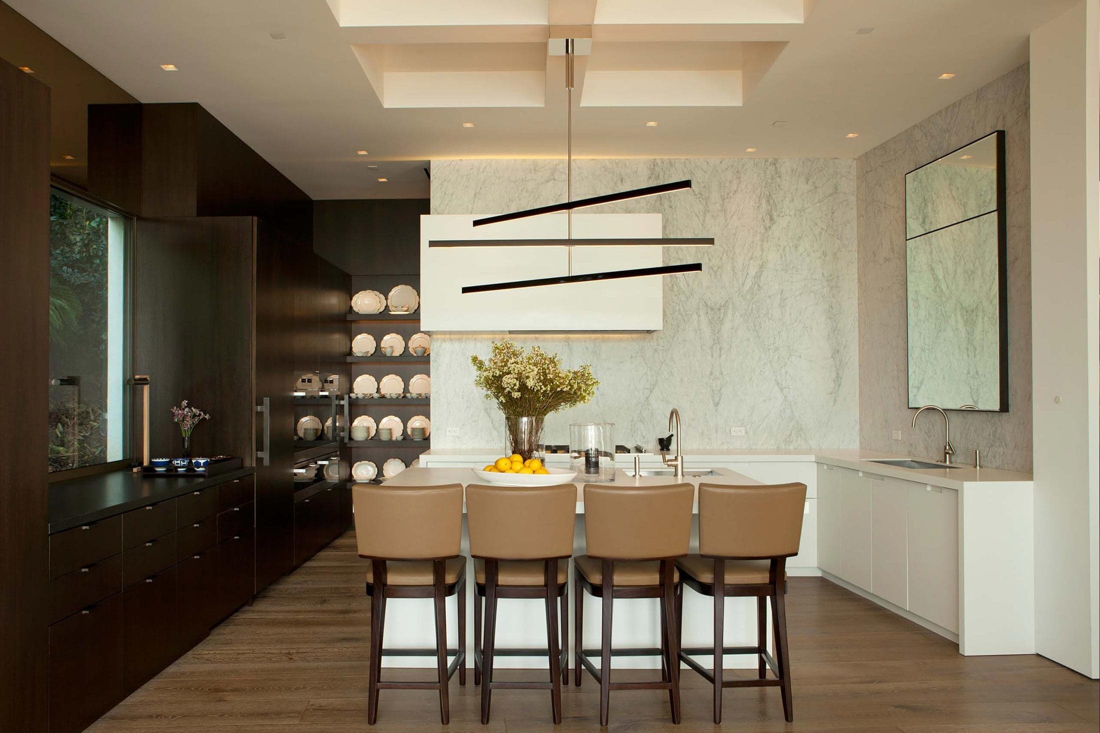 A kitchen with dark wood cabinetry and open shelving facing a marble wall and island