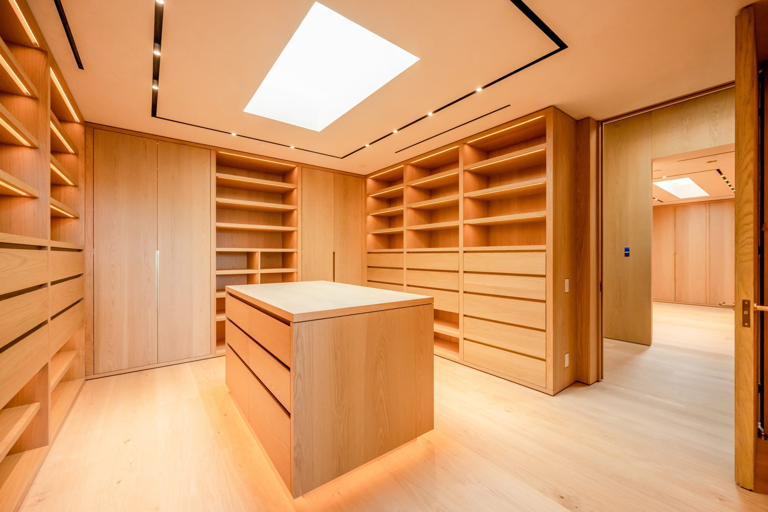 A dressing room of oak drawers and open shelving lit from within, a skylight over the island