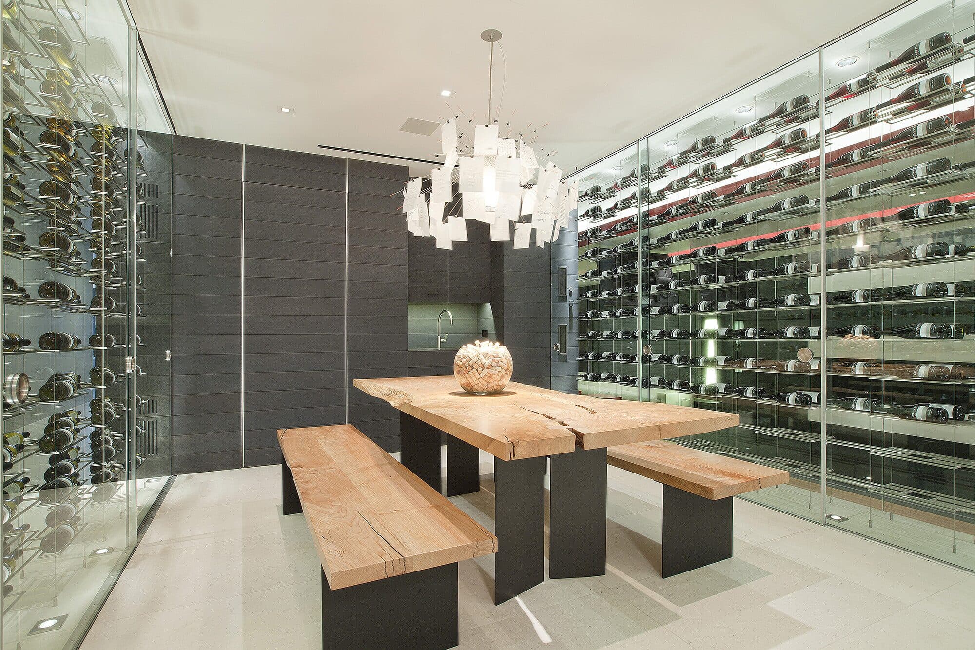 A wine room with glass-fronted racks on both walls and a live-edge table with benches