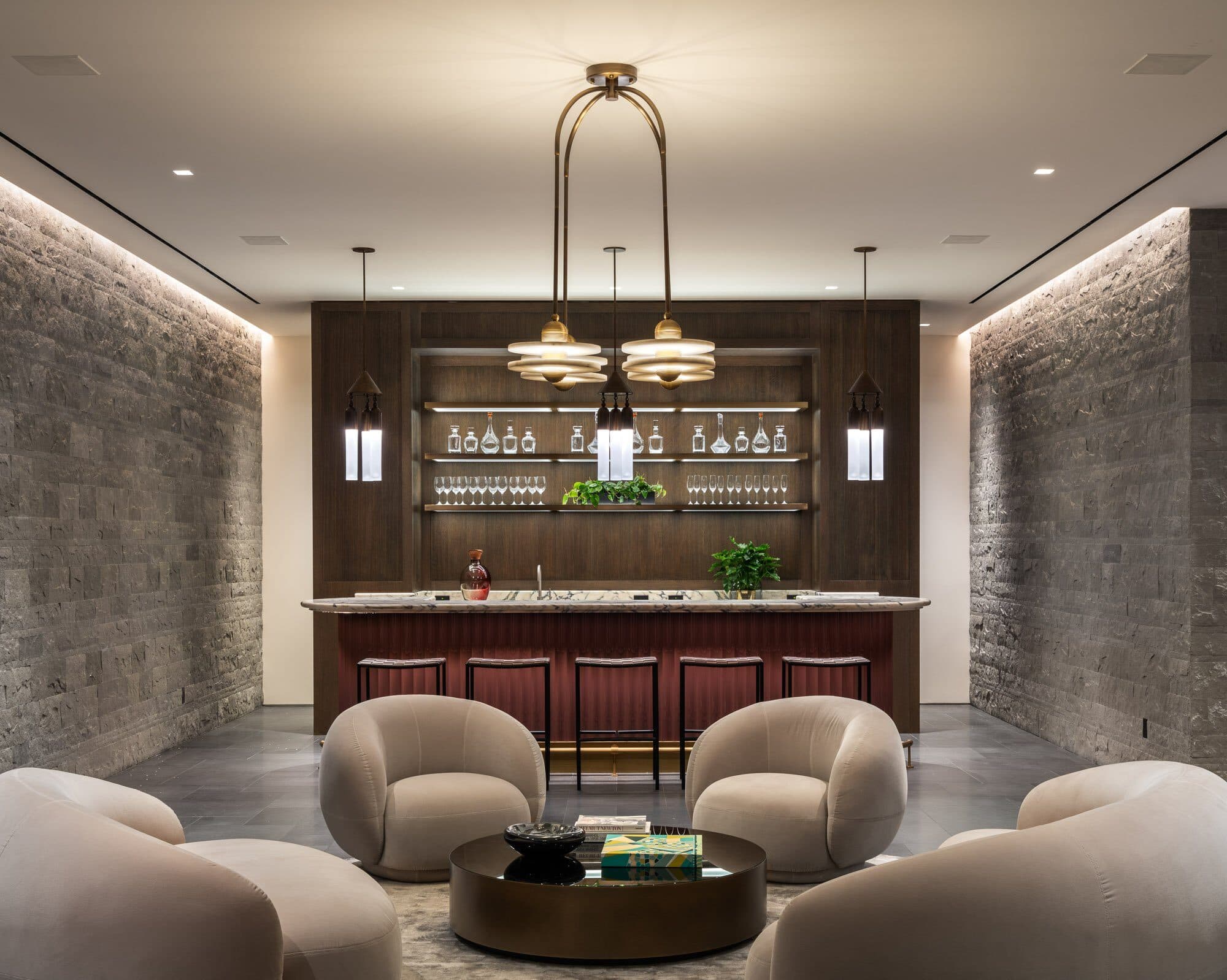 A lounge between two stone walls, a curved bar and lit back-bar shelving at the far end