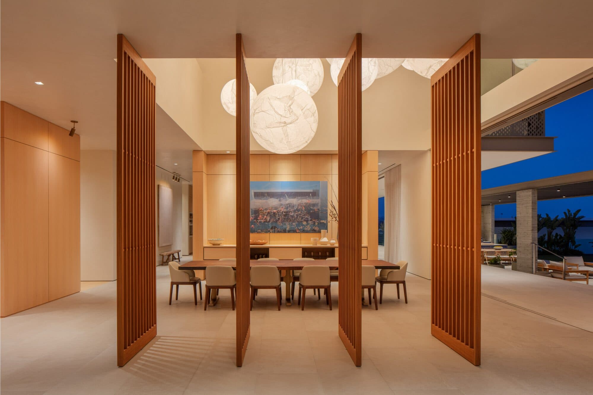 A dining room framed by tall slatted wood screens that pivot open, a long table beyond