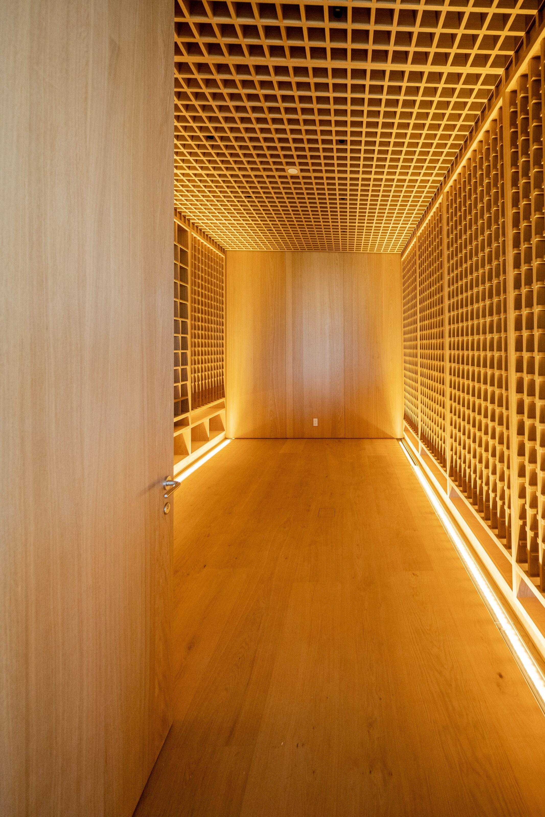 A tall hall walled in a backlit oak lattice, light falling through it onto the floor