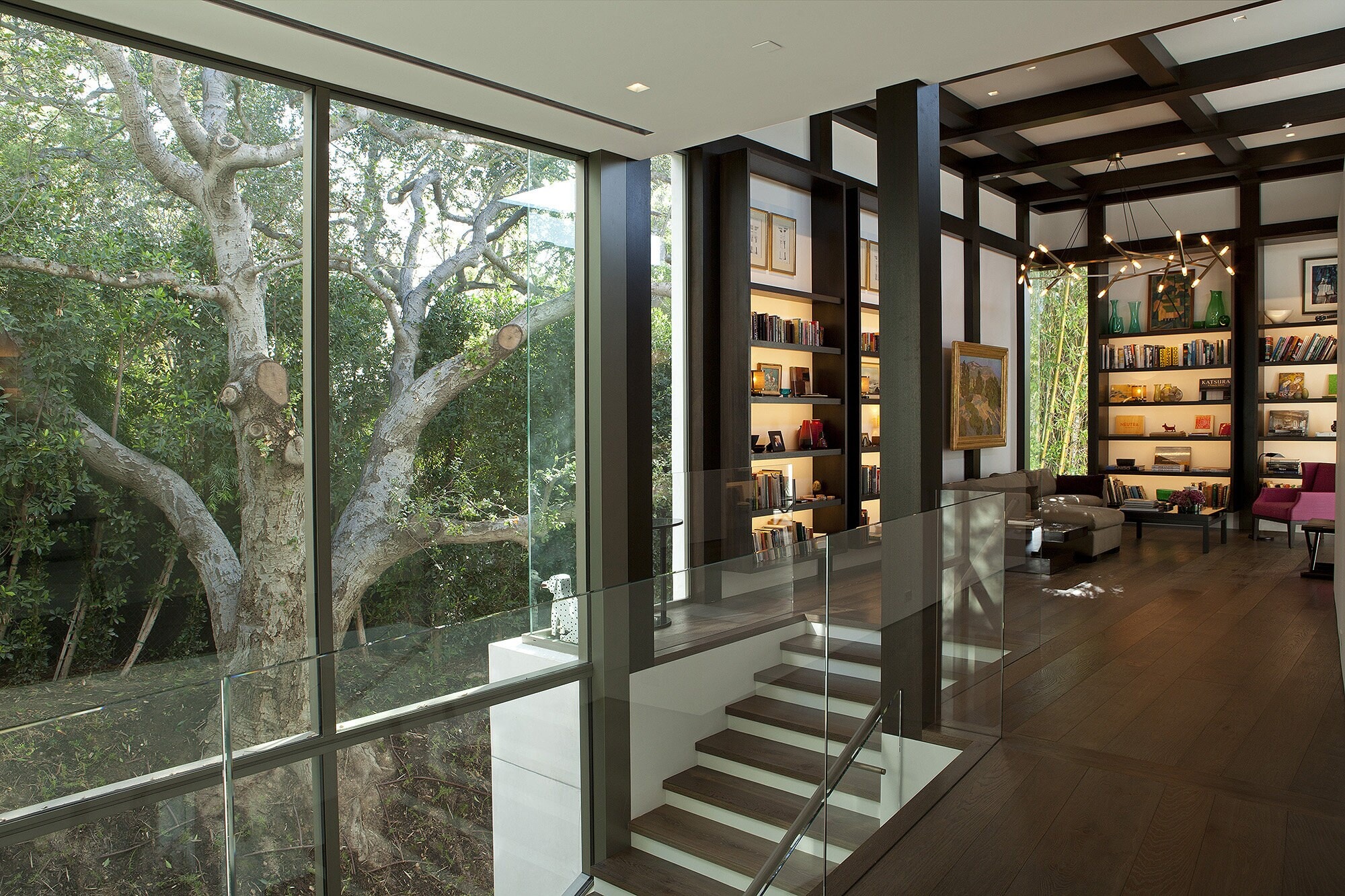 A double-height library of lit dark wood shelving behind a glass stair
