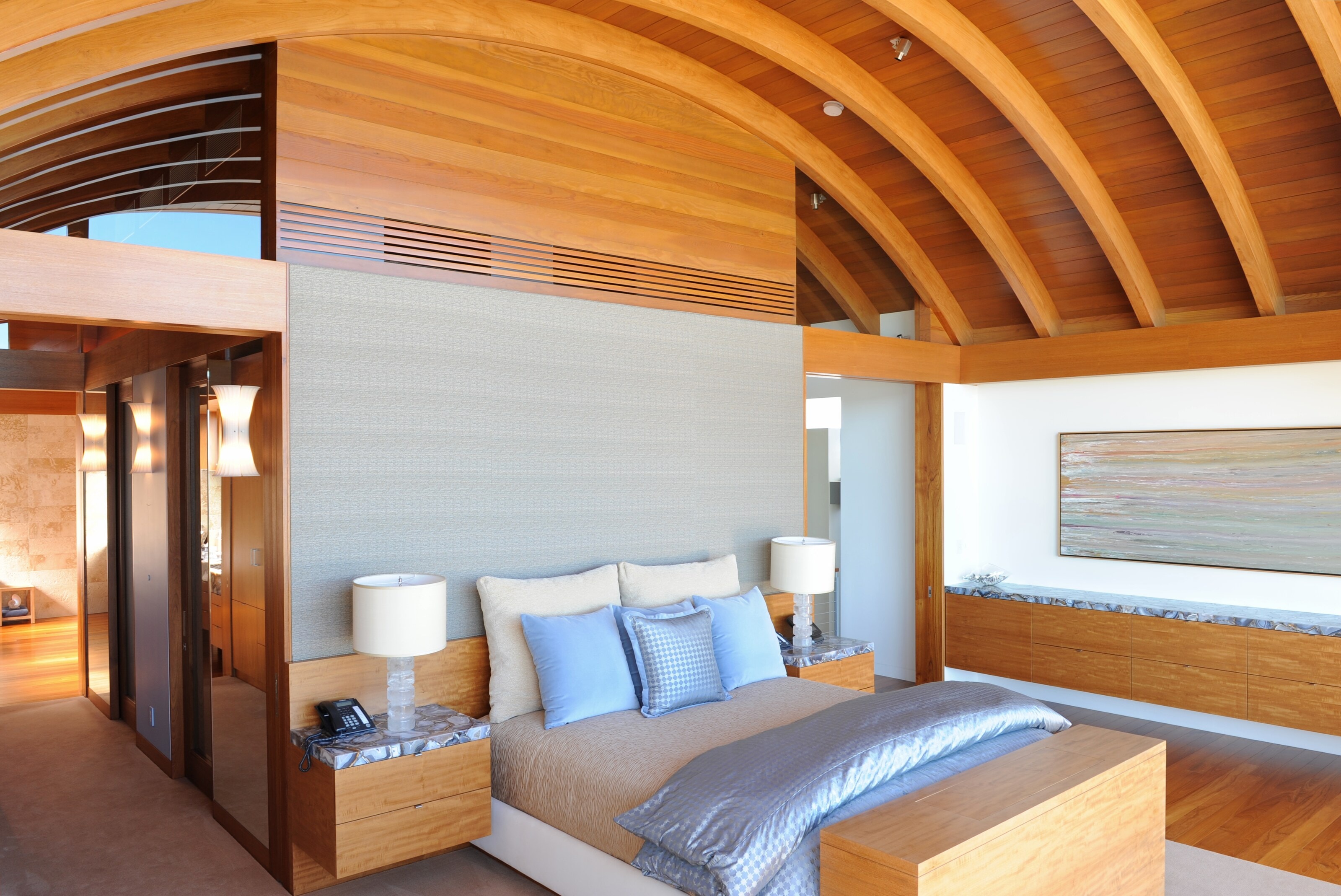 A bedroom under a vaulted ceiling of curved wood ribs, with wood casework along the walls
