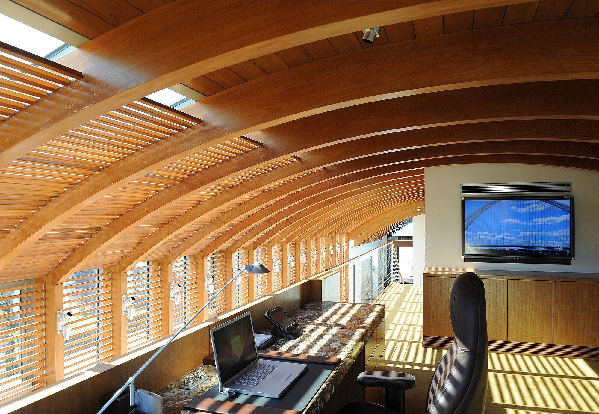 A study under a vaulted ceiling of curved wood ribs, a built-in desk along the windows