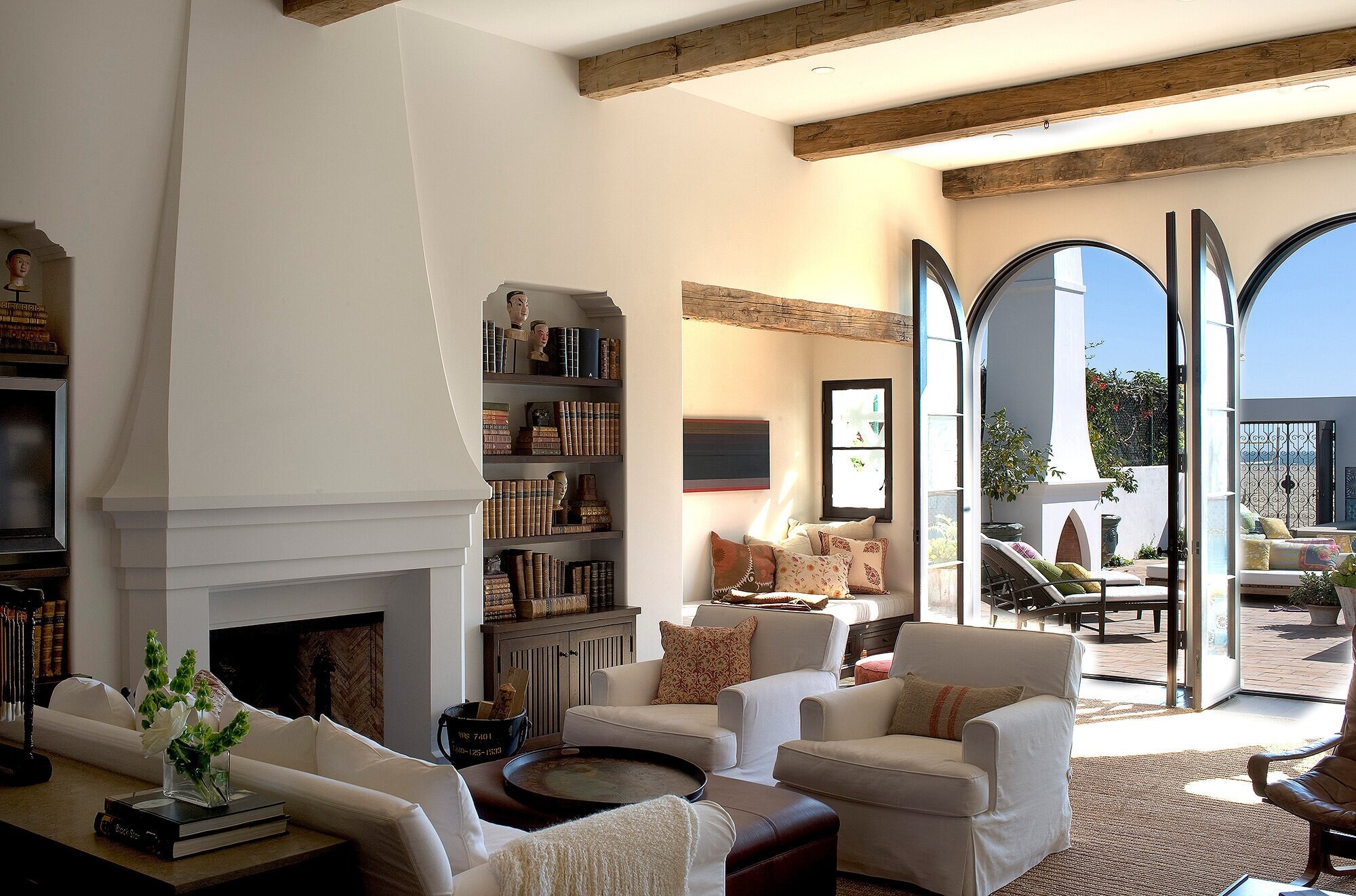 A living room with built-in shelving beside a plaster fireplace and arched doors