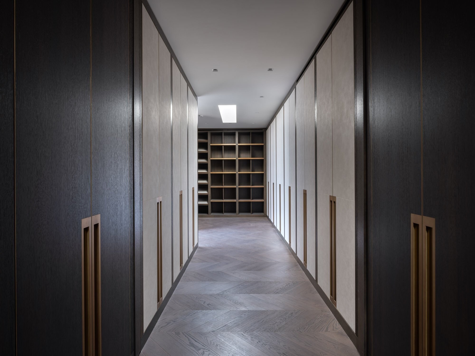 A hall of tall dark wood wardrobe doors leading to lit shelving at the end