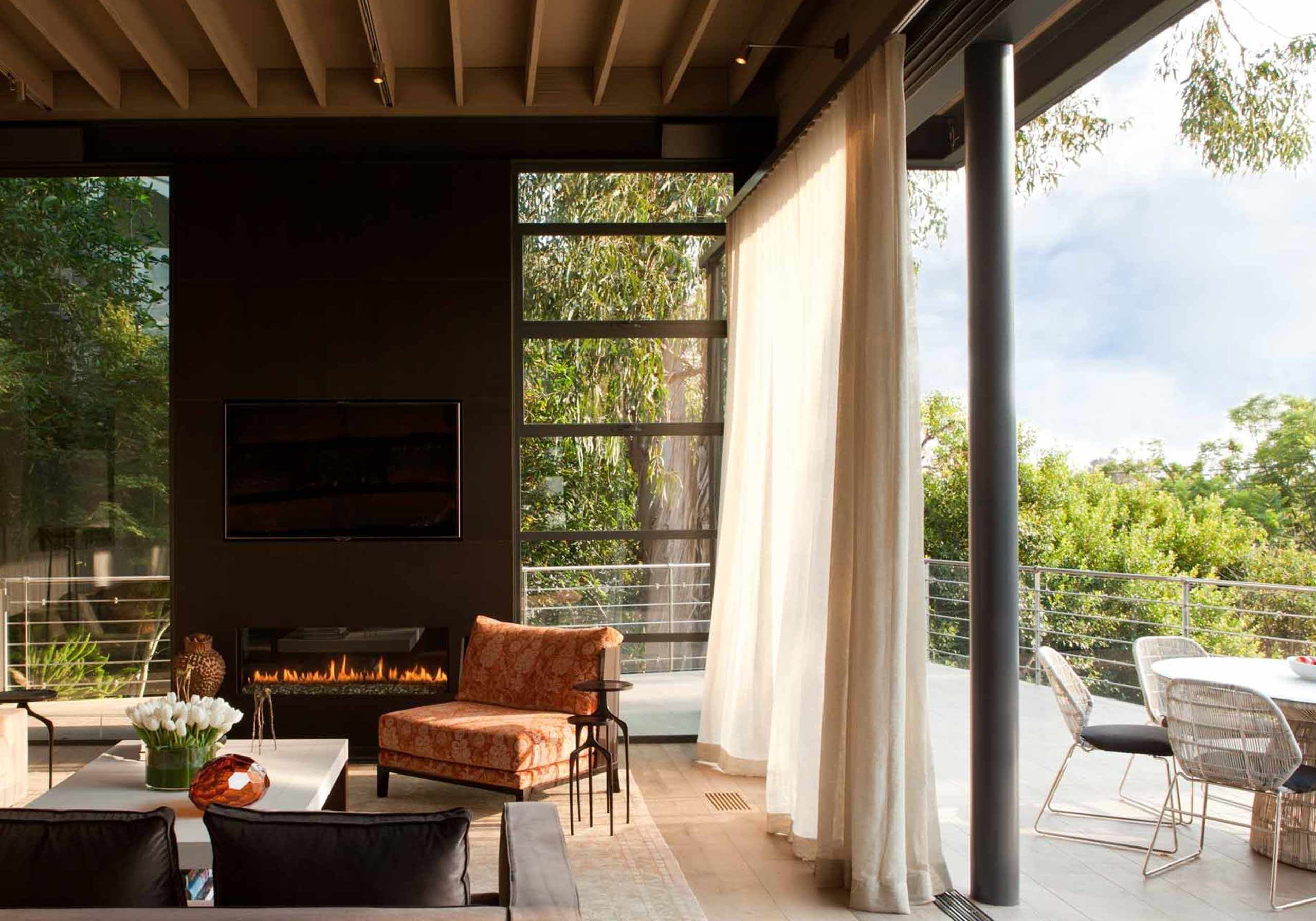 A living room with a dark wood wall and fireplace, garden beyond the glass
