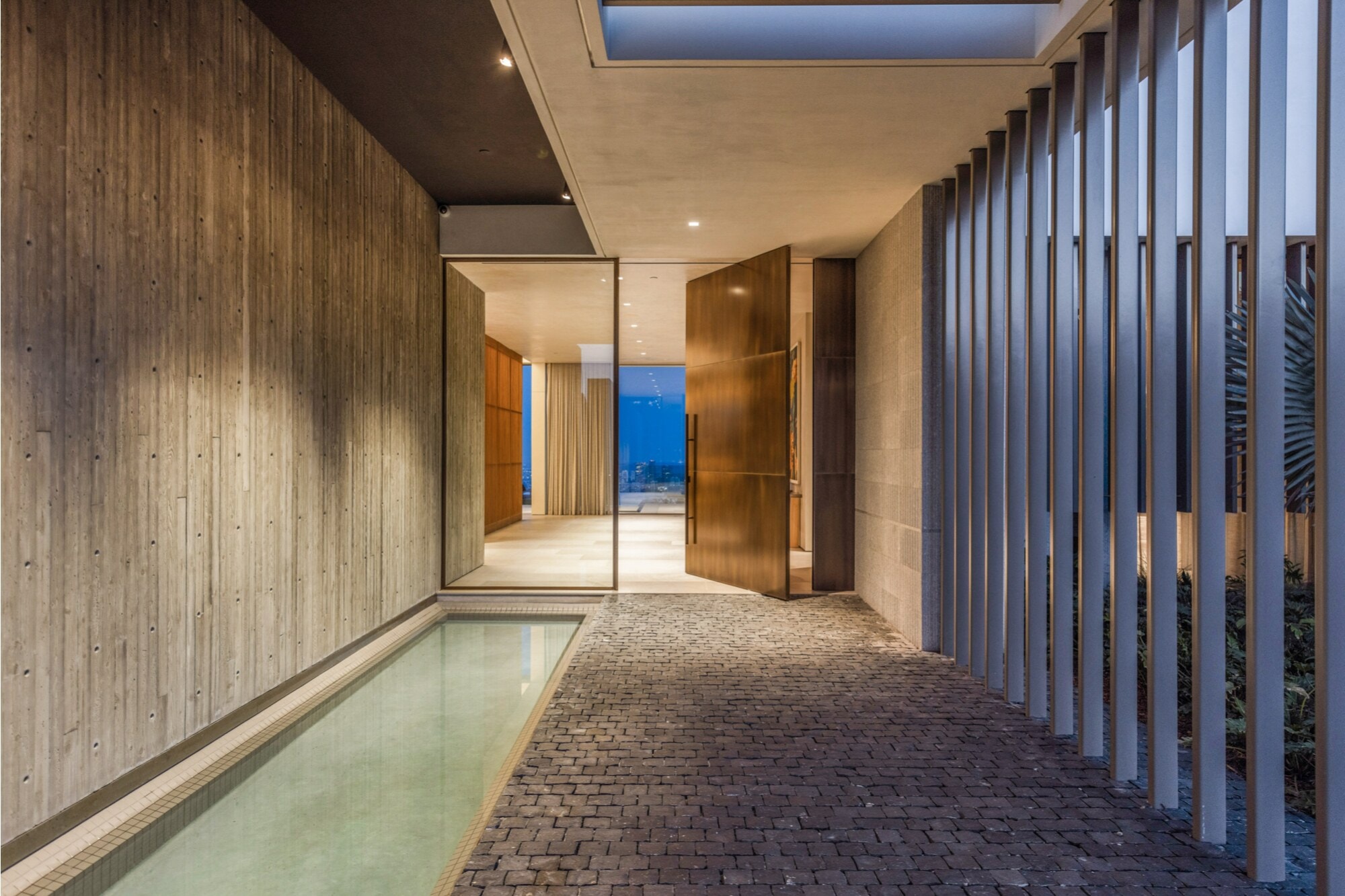 An entry walk between vertical wood fins and a reflecting pool