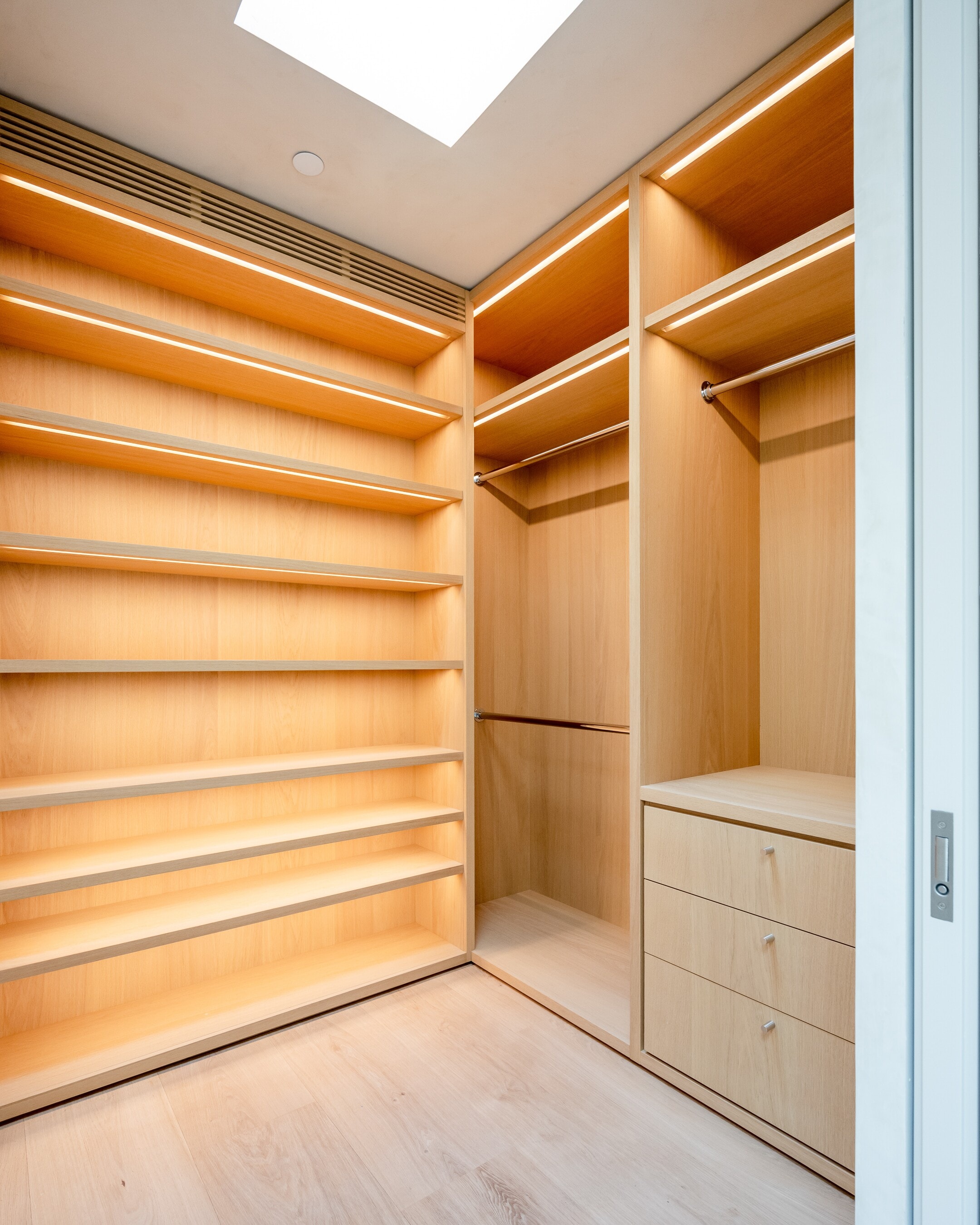 A finished white oak walk-in closet, its shelves lit beneath a skylight