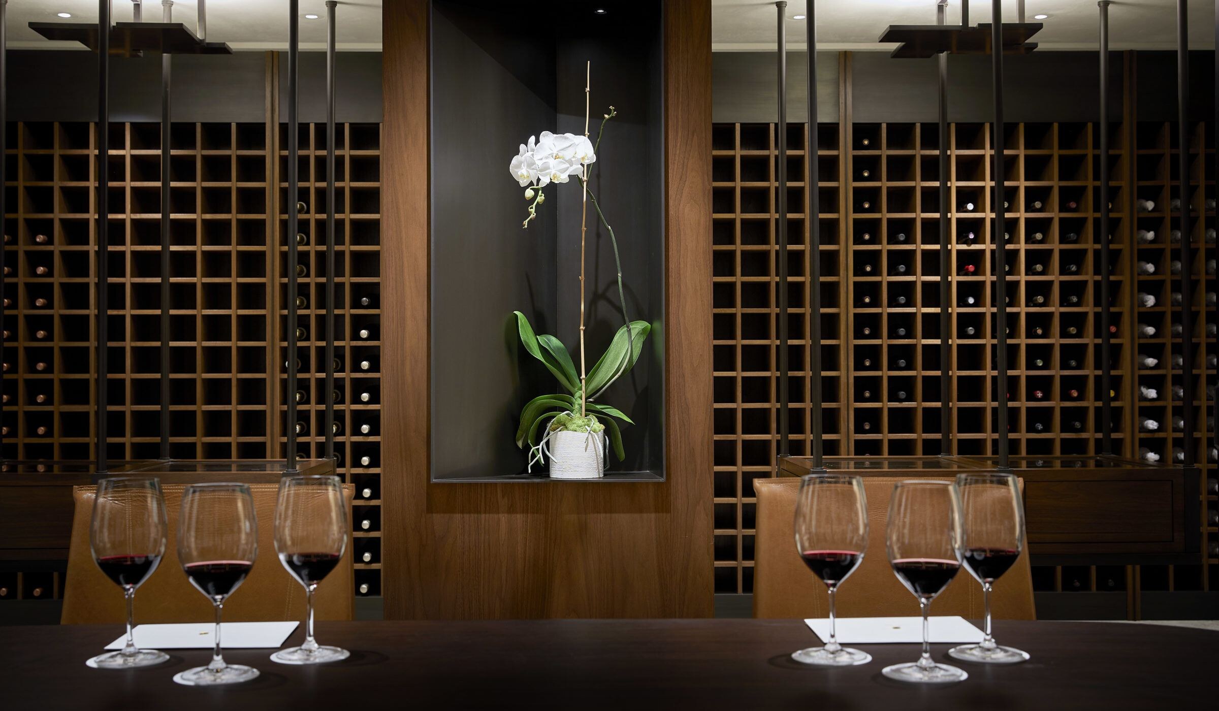 A tasting table before a wall of walnut wine racks, an orchid in a lit niche at its center