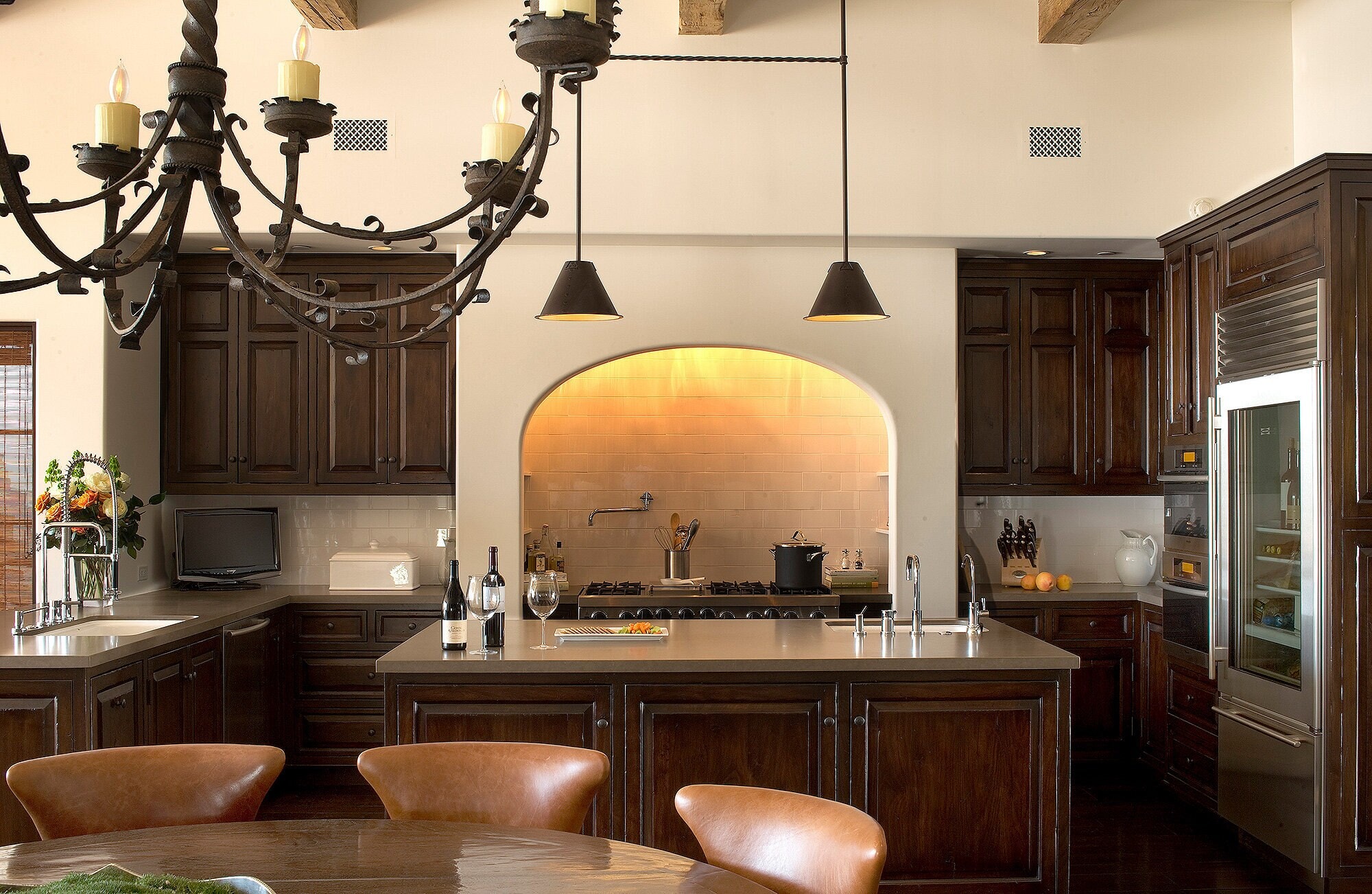 A kitchen of dark stained cabinetry around an arched, lit range alcove