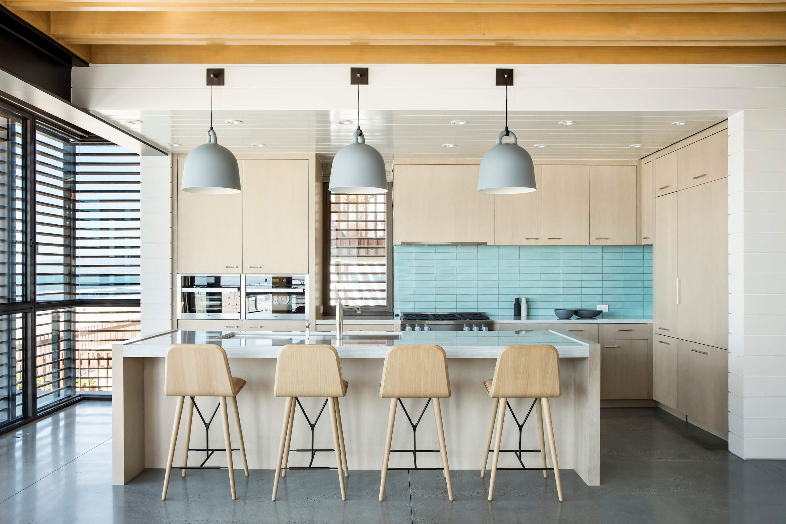 A pale kitchen with a long island under a wood ceiling