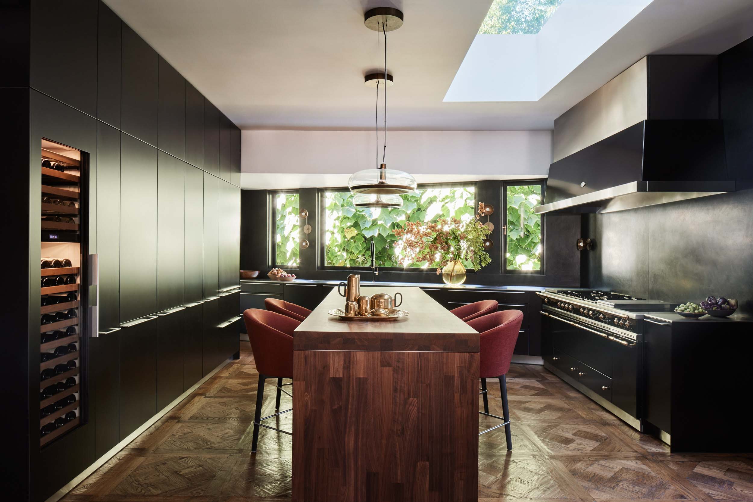 A kitchen of dark walnut cabinetry under a skylight, a long wood island at its center