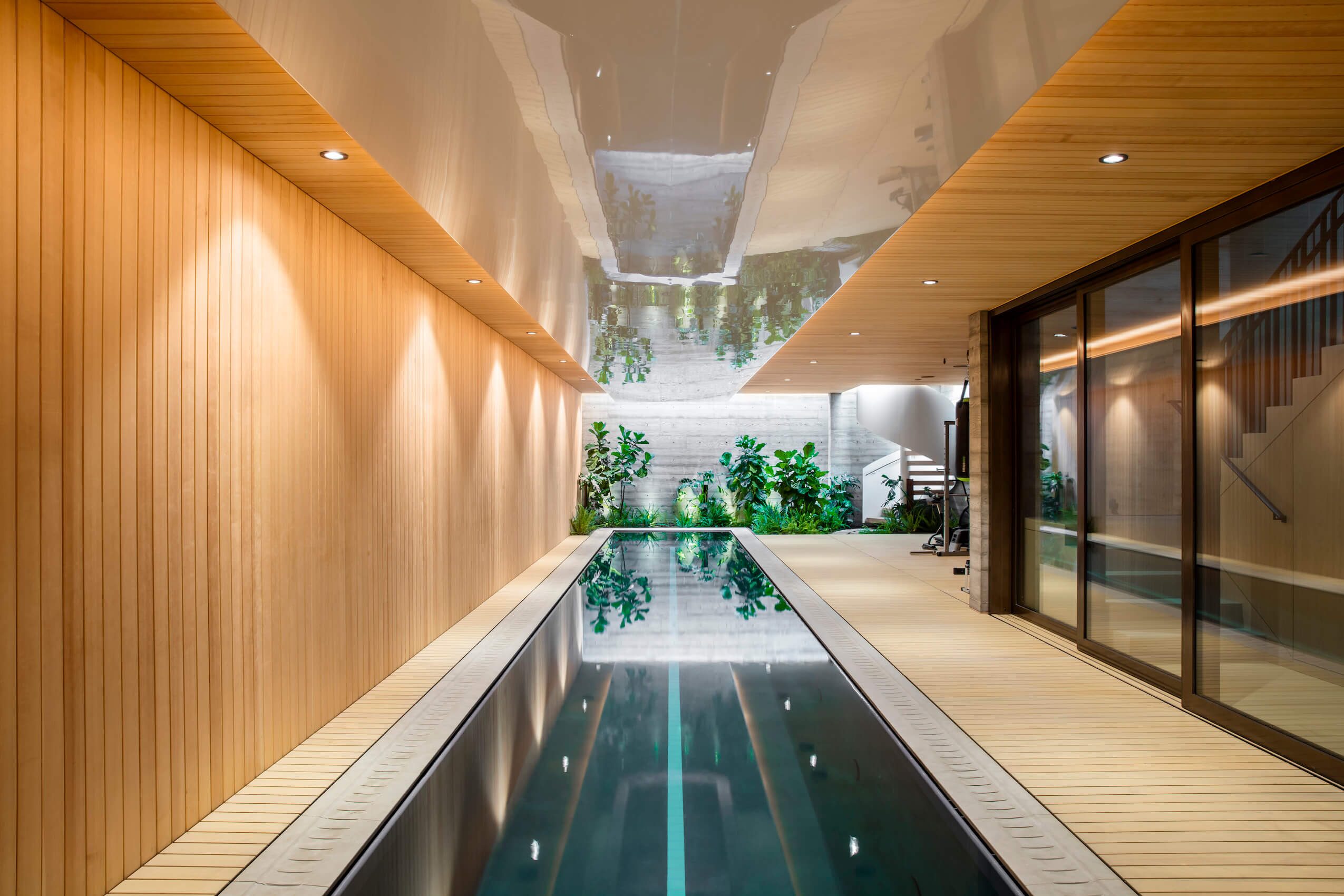 An indoor lap pool running between a wall of vertical wood boards and glass doors